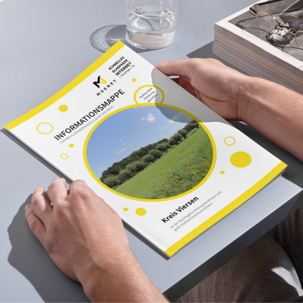 Eine Person hält eine Broschüre mit dem Titel „Informationsmappe Kreis Viersen“ in der Hand. Auf dem Titelbild sind eine grüne Wiese und Bäume unter blauem Himmel zu sehen, daneben ein Glas Wasser und eine Schachtel mit Brillen.