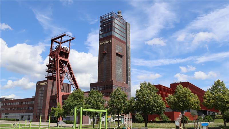 Förderturm und Hochhaus des ehemaligen Bergwerks in Gelsenkirchen vor blauem Himmel mit Wolken