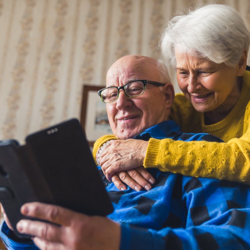Happy caucasian senior couple smiling and hugging while talking to their children on facetime video chat by using a new smartphone. High quality photo
